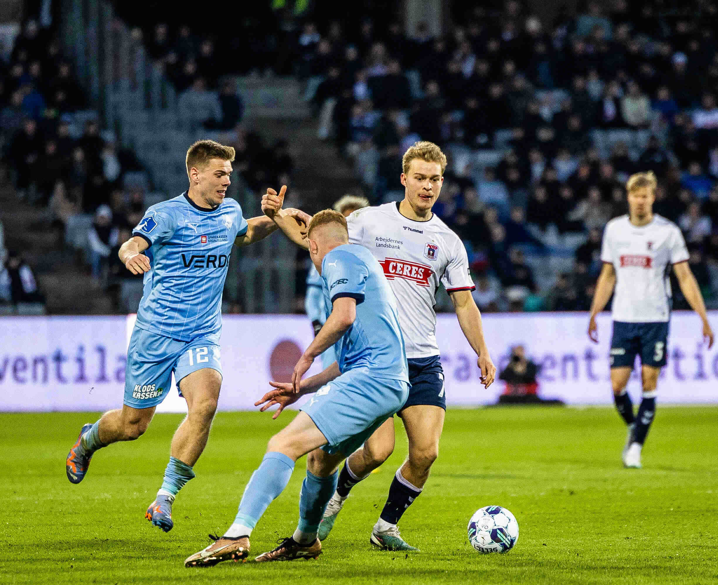 Mads Emil Madsen i hvid AGF trøje i duel med to Randers FC spillere i lyseblå trøjer.