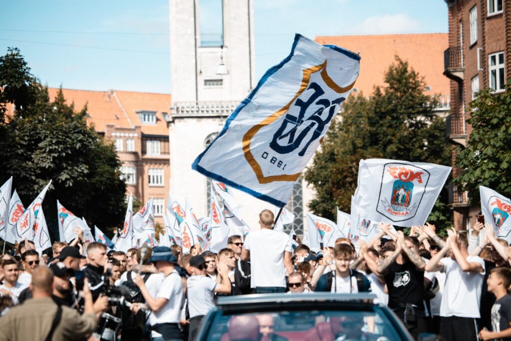Festglade AGF fans synger mens cheftræner Uwe Rösler kører bort i forgrunden.